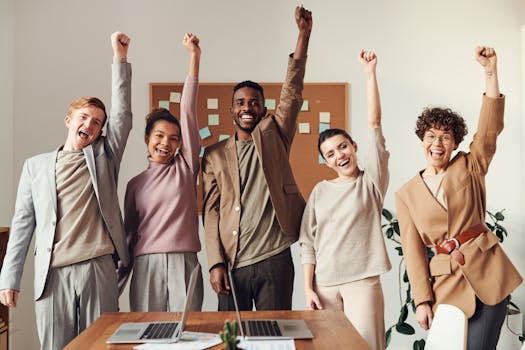 A diverse team celebrating success with raised hands in a modern office setting.